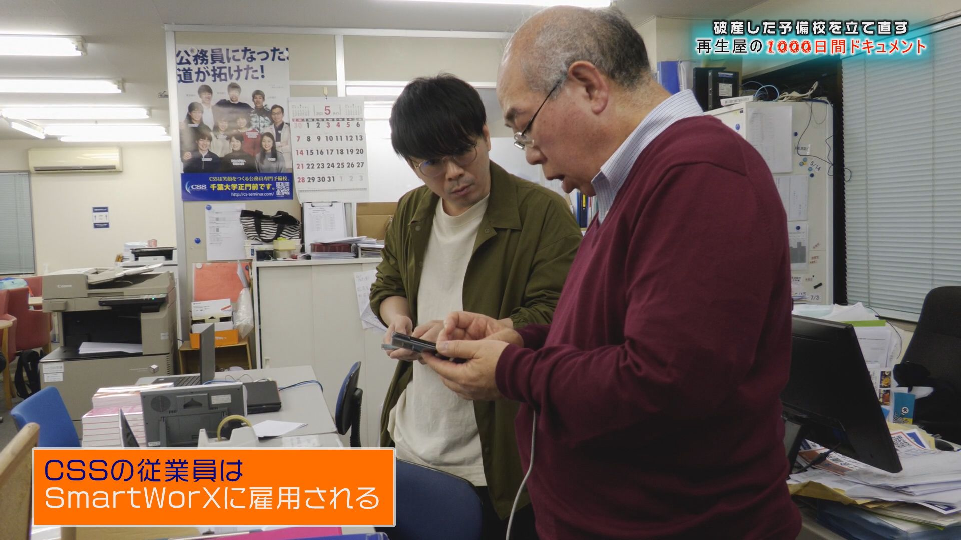 旧予備校のスタッフが新しい経営陣からスマートフォンの使い方を教わる